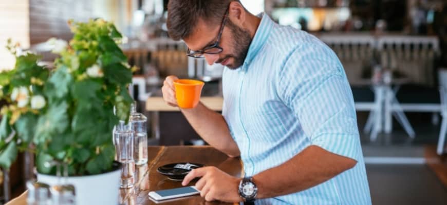 Man looking on his phone while holding his cup of coffee.