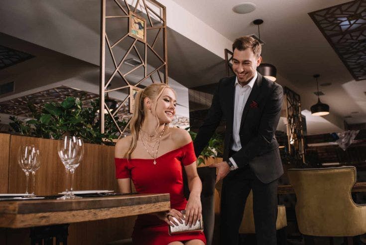 Handsome man helping to sit down attractive woman in red dress